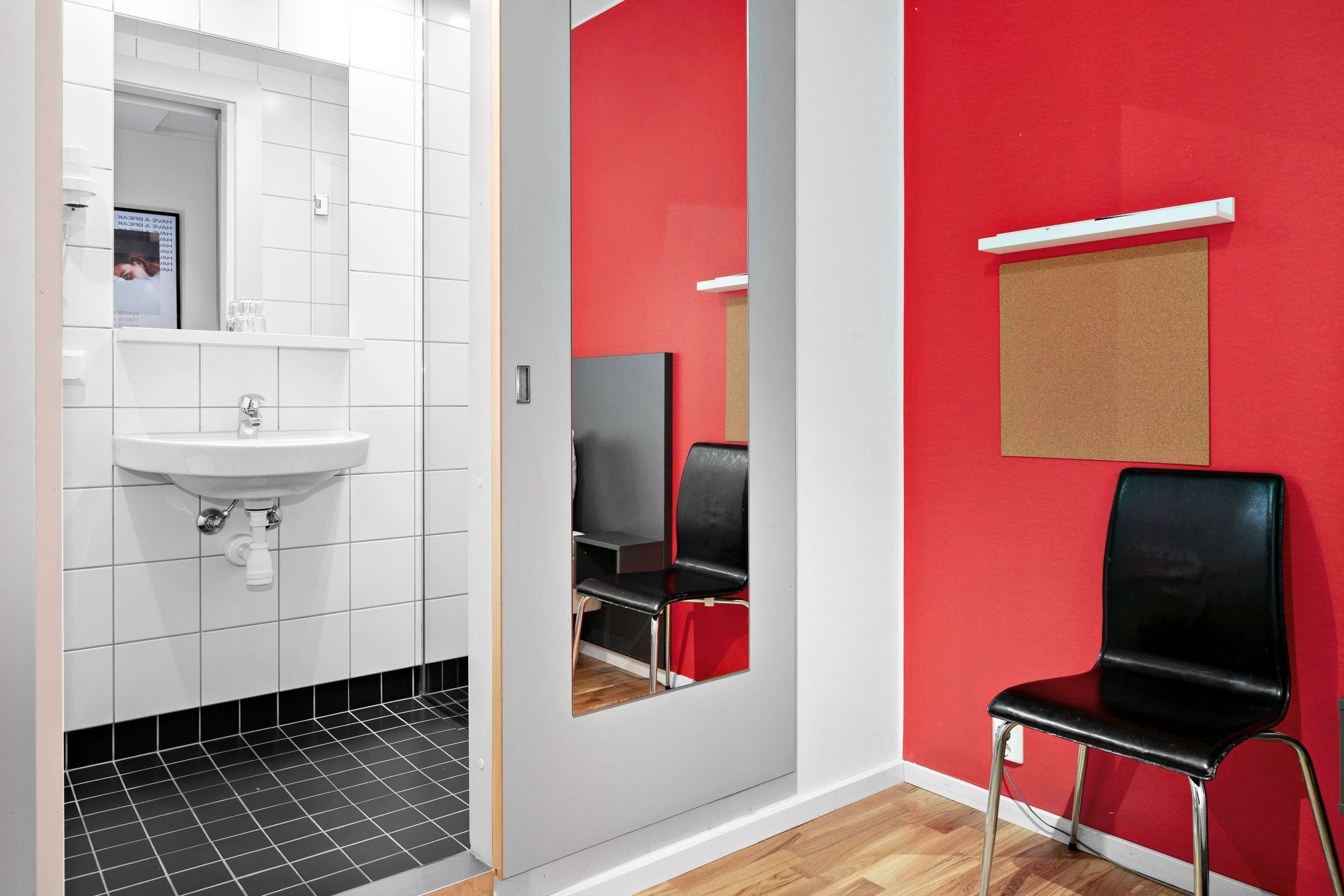 Ein Badezimmer mit weißem Waschbecken, schwarzem Fliesenboden, einer roten Wand und einem schwarzen Stuhl.