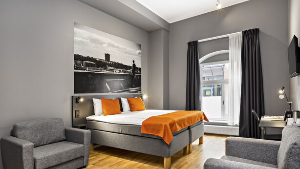 Una habitación de hotel moderna con una cama grande, dos sillones, un escritorio y un cuadro con vista a la ciudad.