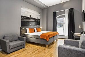 Una habitación de hotel moderna con una cama grande, dos sillones, un escritorio y un cuadro con vista a la ciudad.