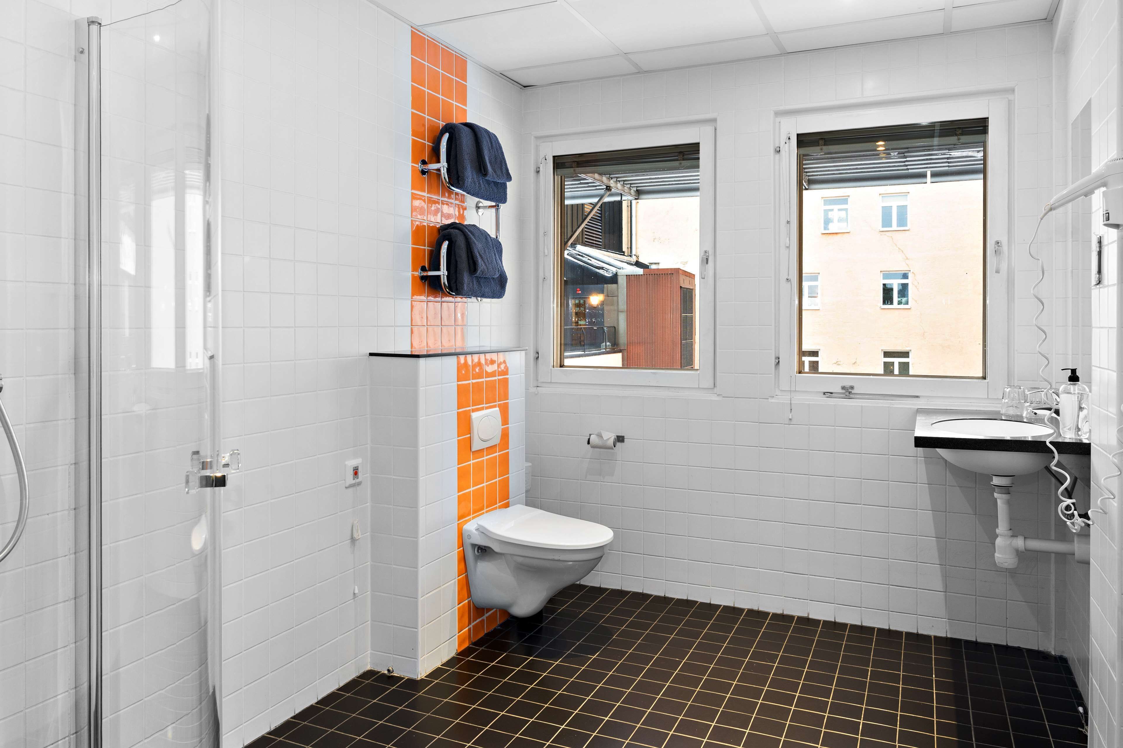 A bathroom with a white toilet, a glass shower enclosure, a window, and a sink.
