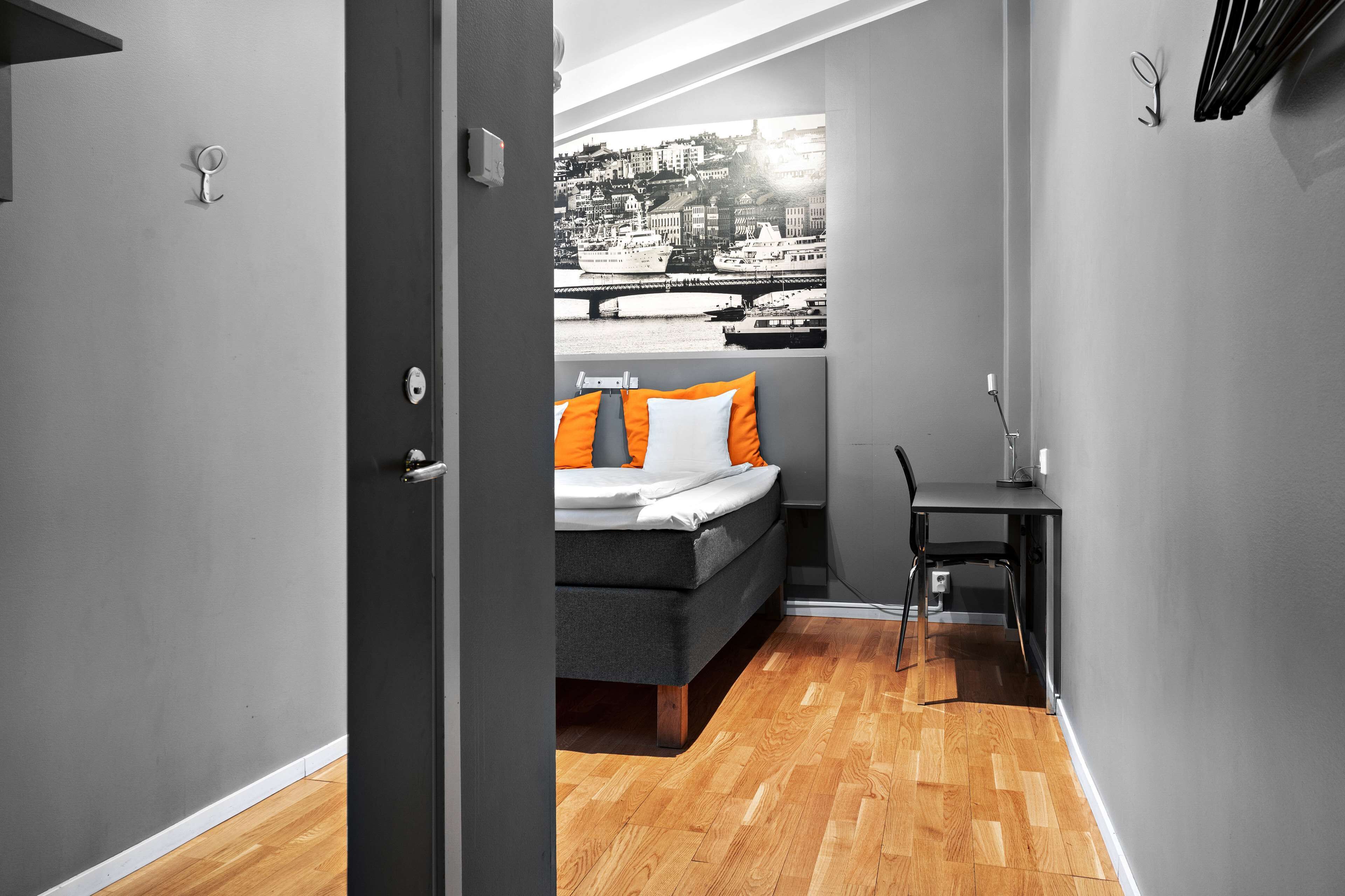 Habitación de hotel estrecha con cama, escritorio y vista a un paisaje urbano por la ventana.
