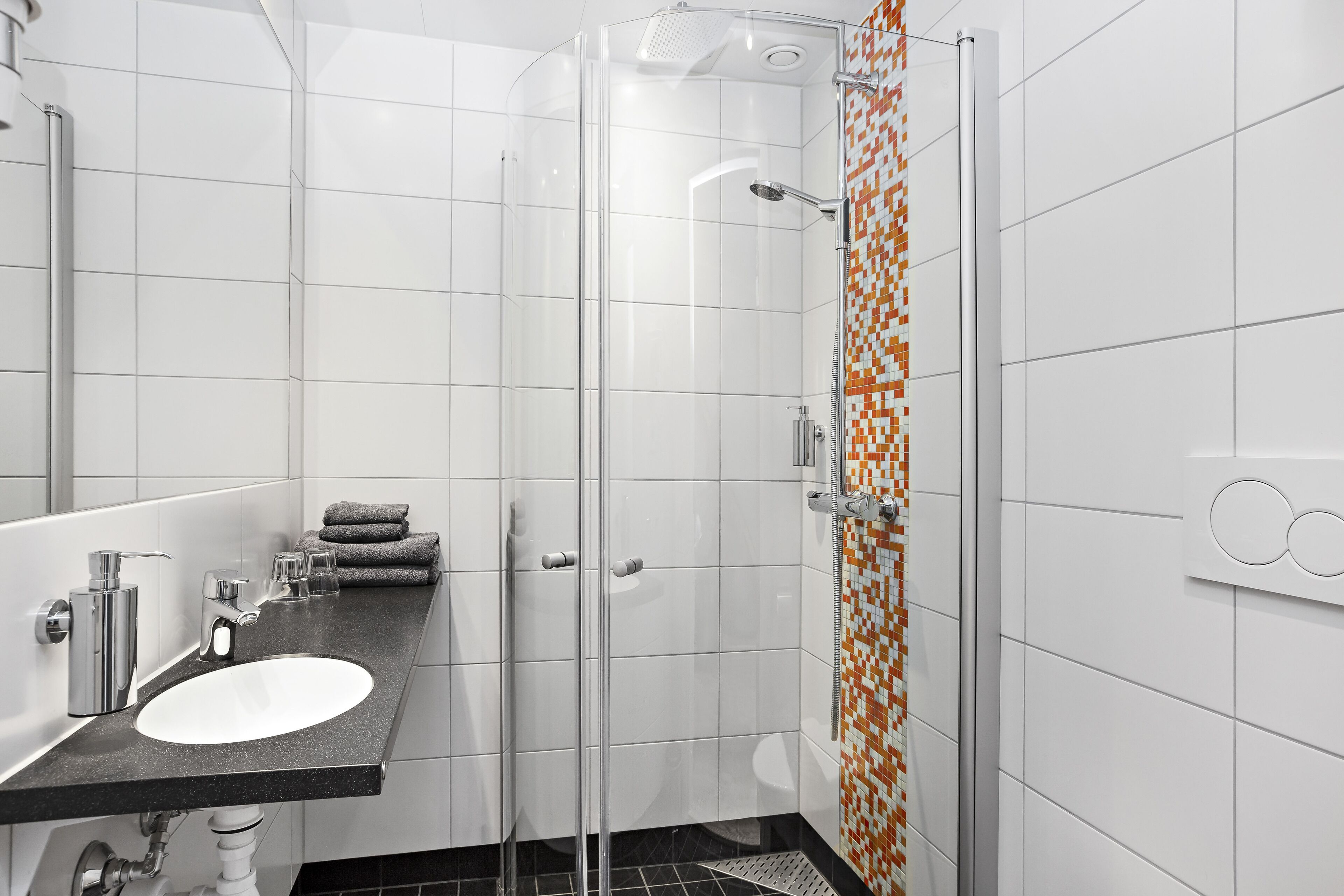 Une salle de bain moderne avec une douche à parois de verre, un lavabo blanc et un sol carrelé.