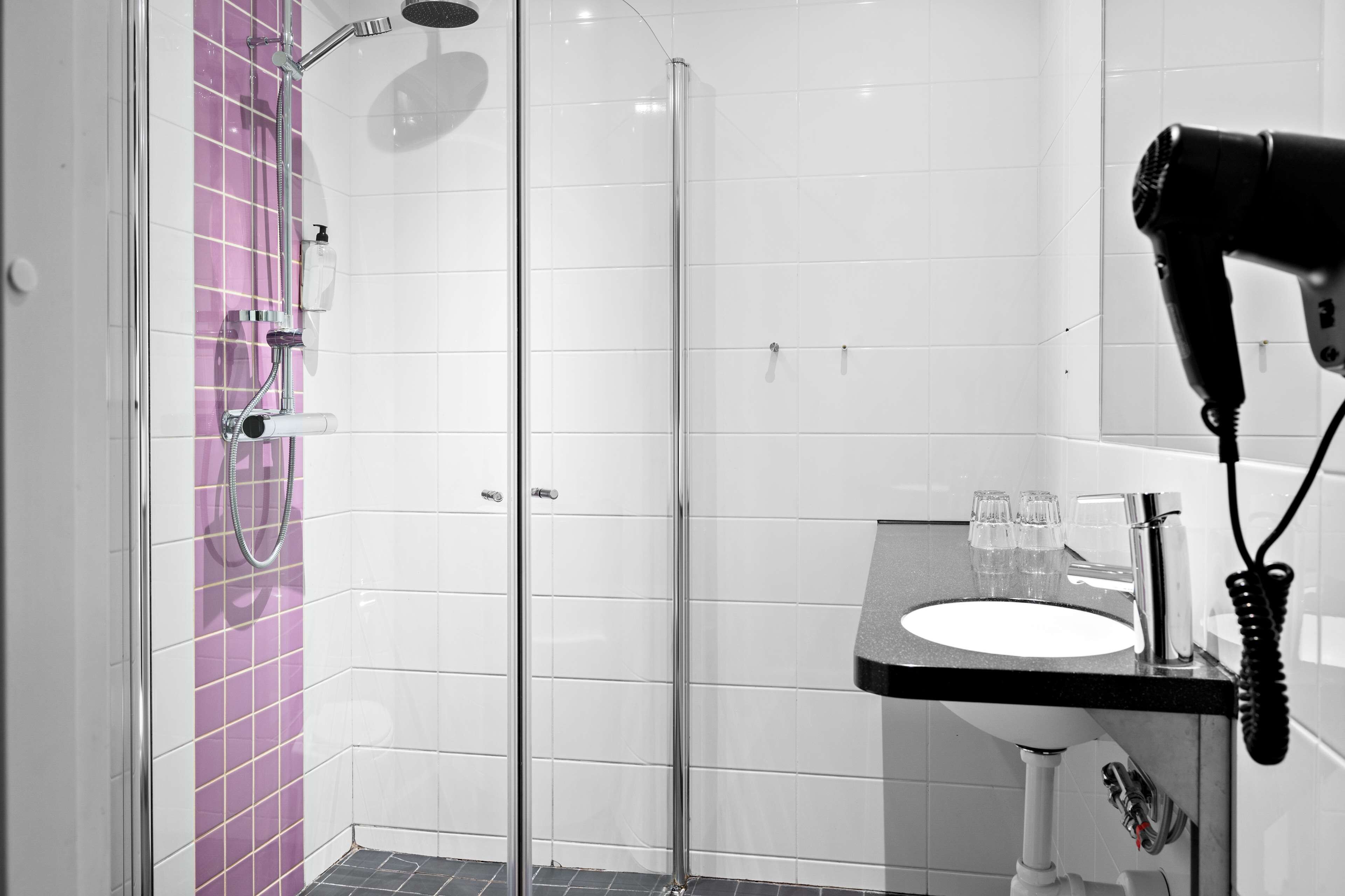 A bathroom with a glass shower enclosure, a sink with a mirror, and a hairdryer on the wall.