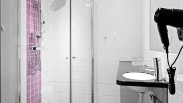 Un baño con cabina de ducha de vidrio, lavabo con espejo y secador de pelo en la pared.