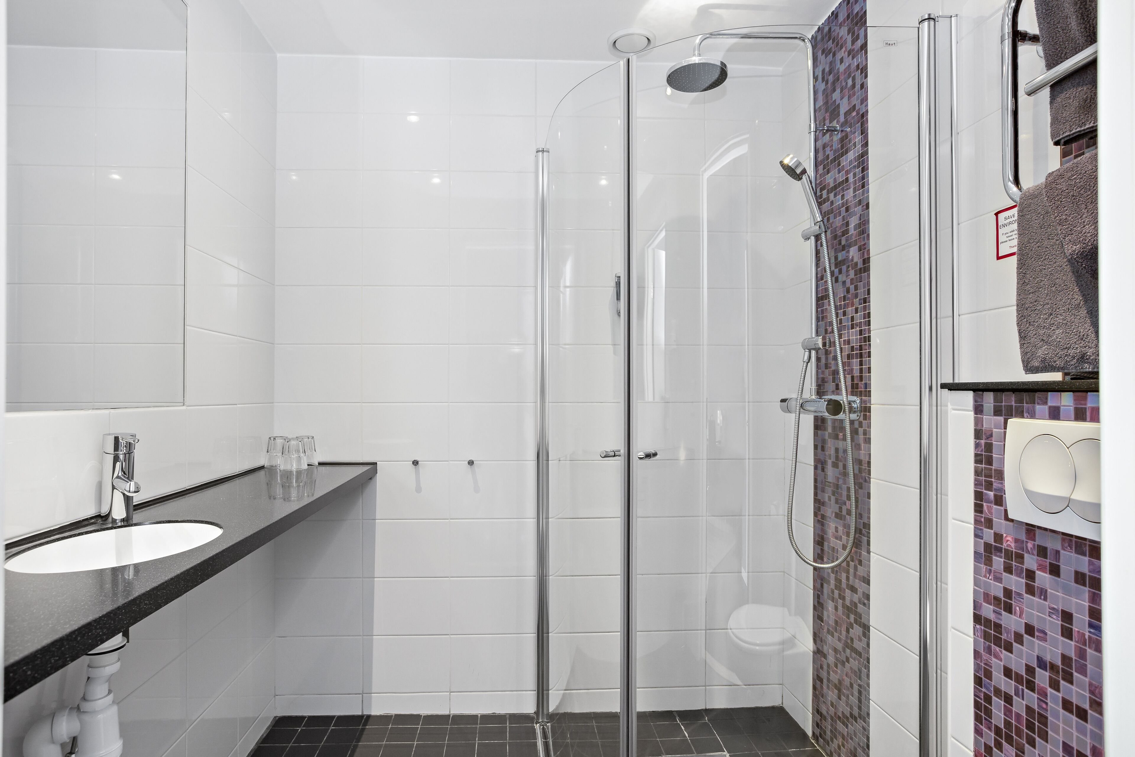 Ein modernes Badezimmer mit einer Duschkabine, einem weißen Waschbecken und gefliestem Boden.
