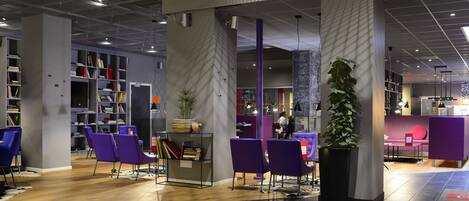 A modern library with purple chairs, bookshelves, and a large plant.
