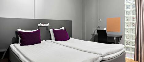Una habitación de hotel moderna con una cama grande, dos almohadas moradas, un escritorio y una ventana con cortinas.