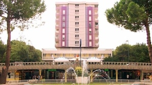 A multi-story building with a central fountain, surrounded by trees and a pedestrian walkway.