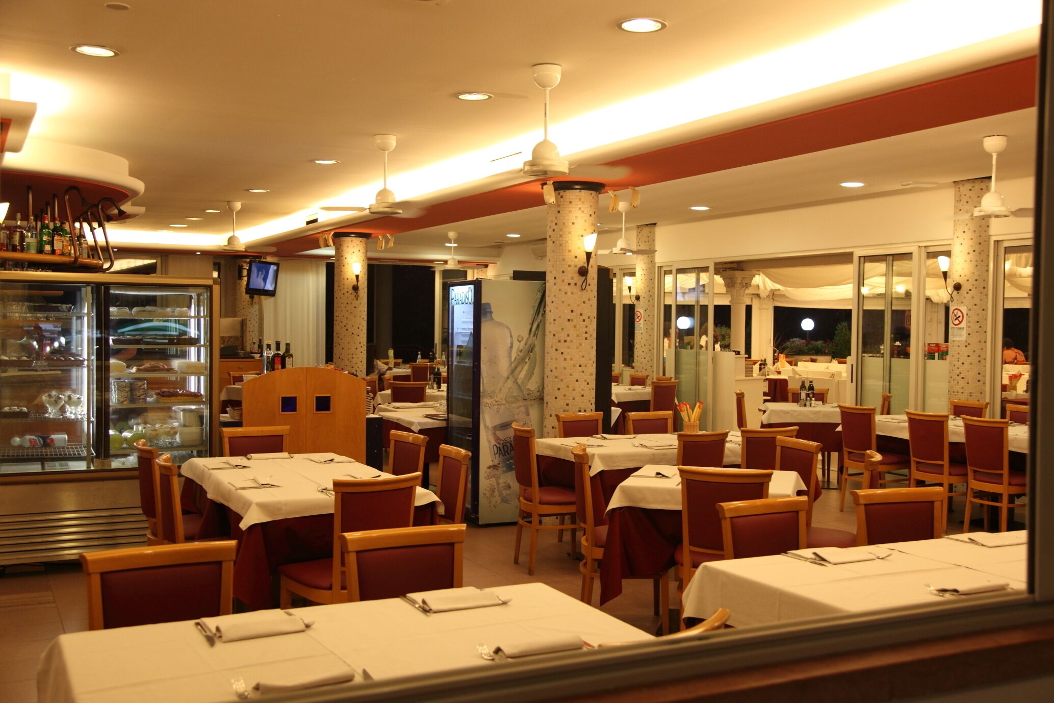 En restaurant med flere borde og stole, en kagedisk og et fjernsyn.