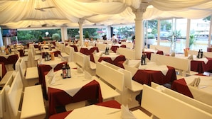 A restaurant with white tables and red tablecloths, large windows, and a view of the outdoors.
