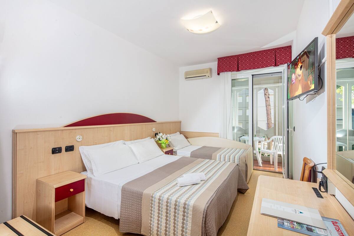 A hotel room with a wooden bed, a desk with a chair, a TV, and a sliding glass door to the outside.