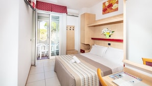 A hotel room with a bed, a desk with a chair, a wardrobe, and a sliding glass door leading to an outdoor area with chairs.