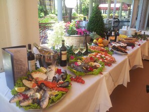 A table set with seafood, wine, and fruits, indicating a dining area with a view of the outdoors. - Regina (Lignano Sabbiadoro)