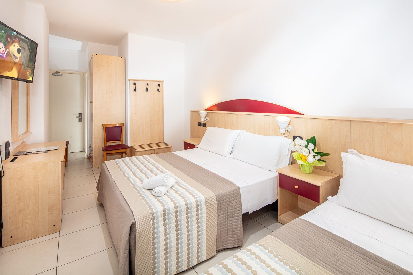 A hotel room with a bed, a desk, a chair, a wardrobe, and a TV.