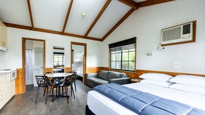 Een kamer met een bed, een eettafel met stoelen, een bank en een raam met jaloezieën.