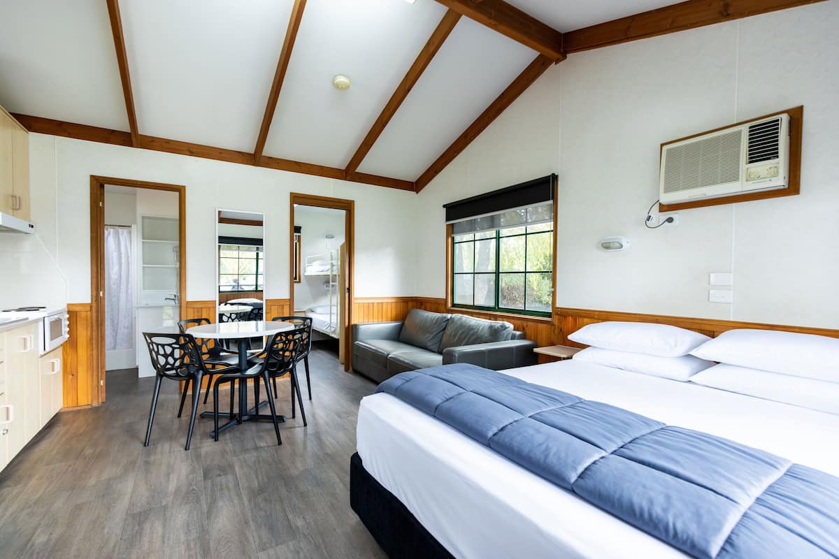 A room with a bed, a dining table with chairs, a sofa, and a window with blinds.
