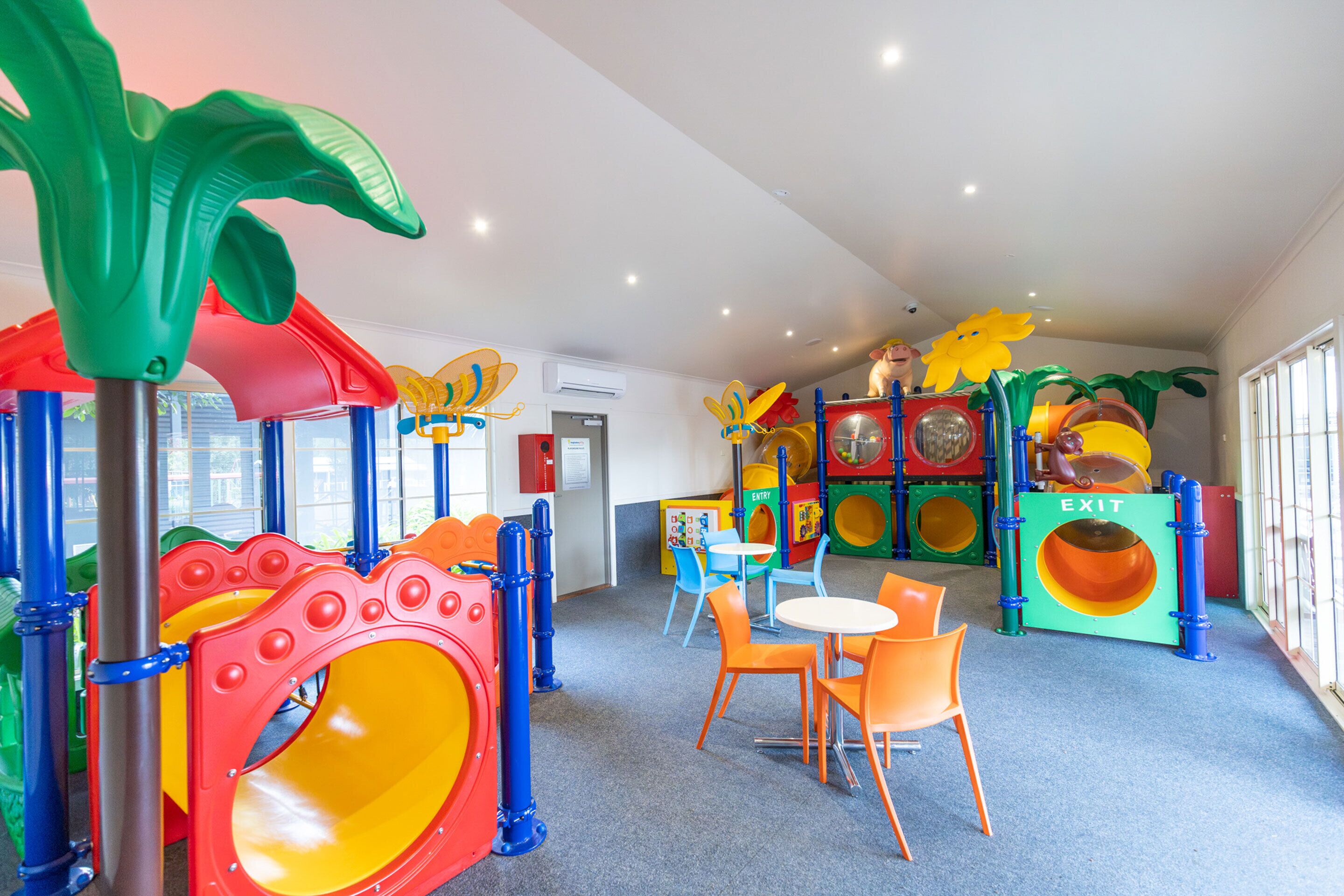 Un espace de jeux pour enfants avec des structures colorées, des sièges et un panneau indiquant la sortie.