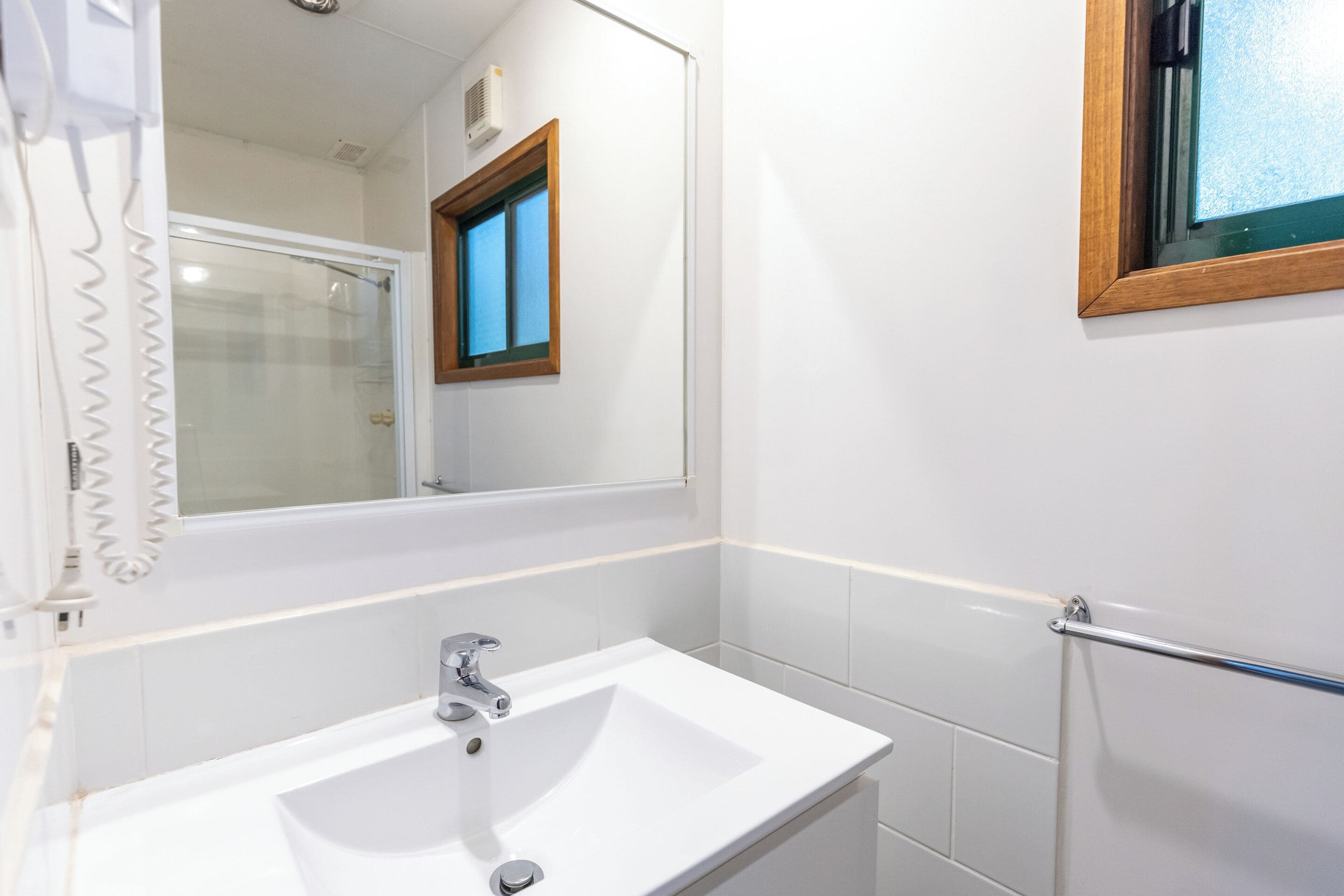 Un bagno con un lavandino bianco, uno specchio e una finestra con cornice in legno.