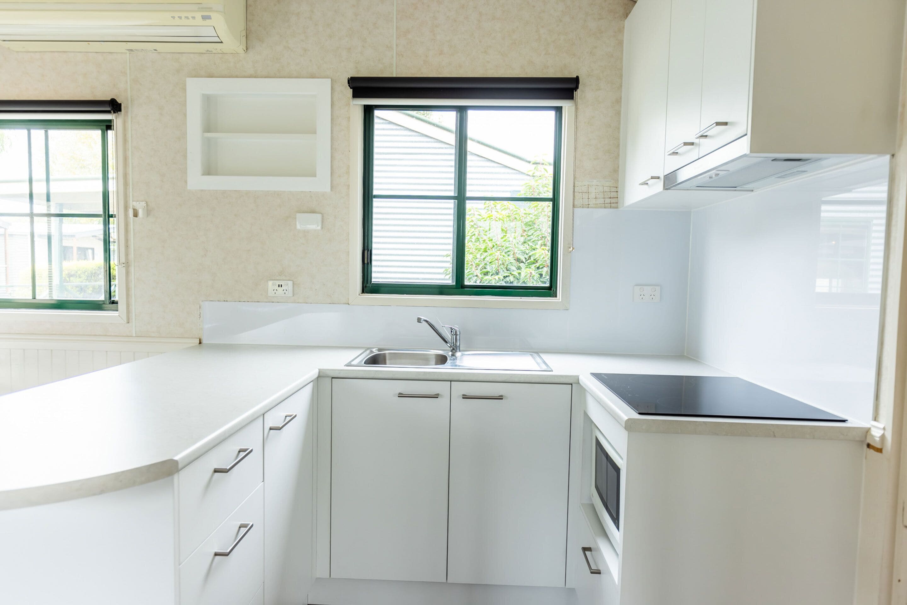 A modern kitchen with white cabinets, a built-in microwave, and a window with blinds.