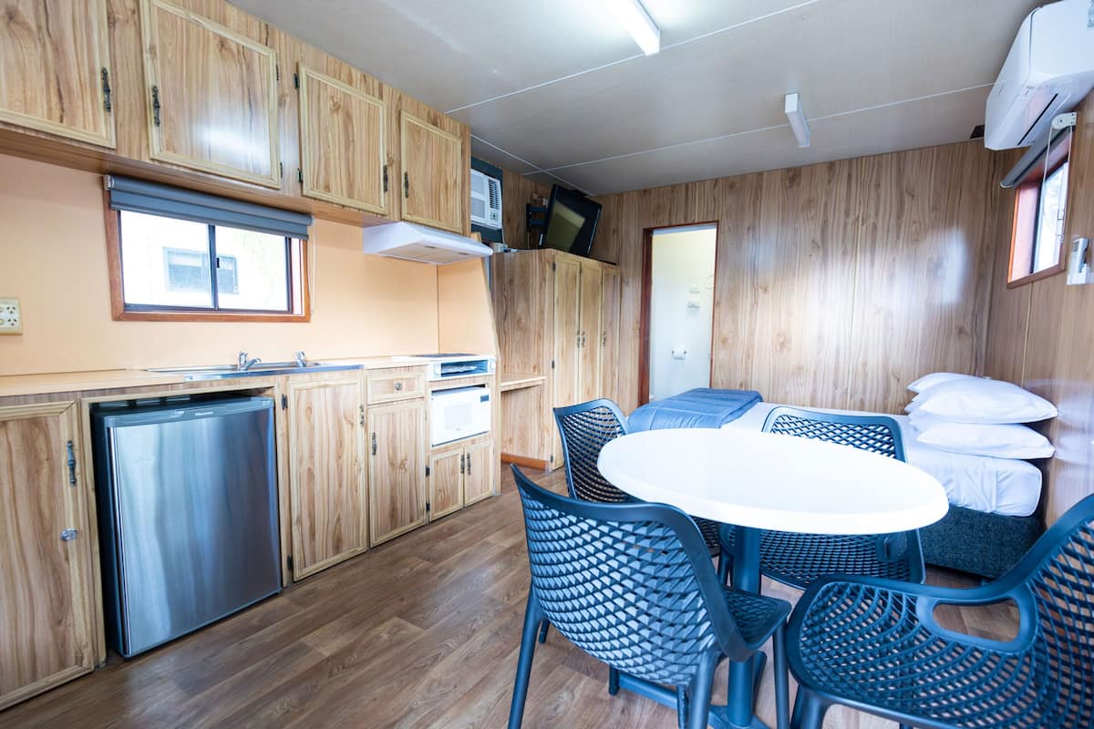 A compact kitchen with wooden cabinets, a built-in dishwasher, and a dining area with a round table and blue chairs.