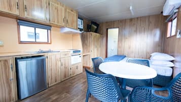 A compact kitchen with wooden cabinets, a built-in dishwasher, and a dining area with a round table and blue chairs.