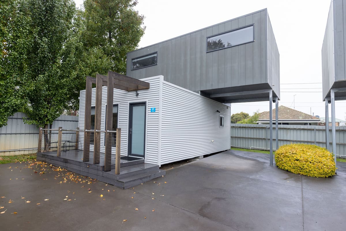 A modern building with a metal exterior, a covered outdoor area with a bench, and a small garden.