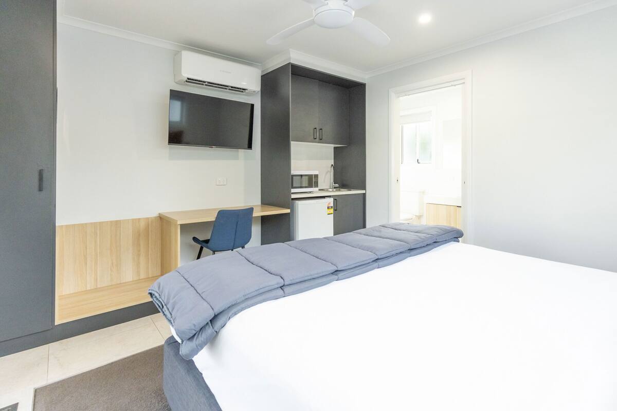 A modern hotel room with a bed, a desk, a chair, and a TV mounted on the wall.