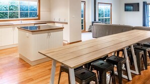 Een moderne keuken met een houten aanrecht en barstoelen, een eettafel en een groot raam met uitzicht op een bebost gebied.