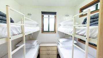 Un dormitorio tipo camarote con dos camas, una ventana pequeña y una mesita de noche con cajones.