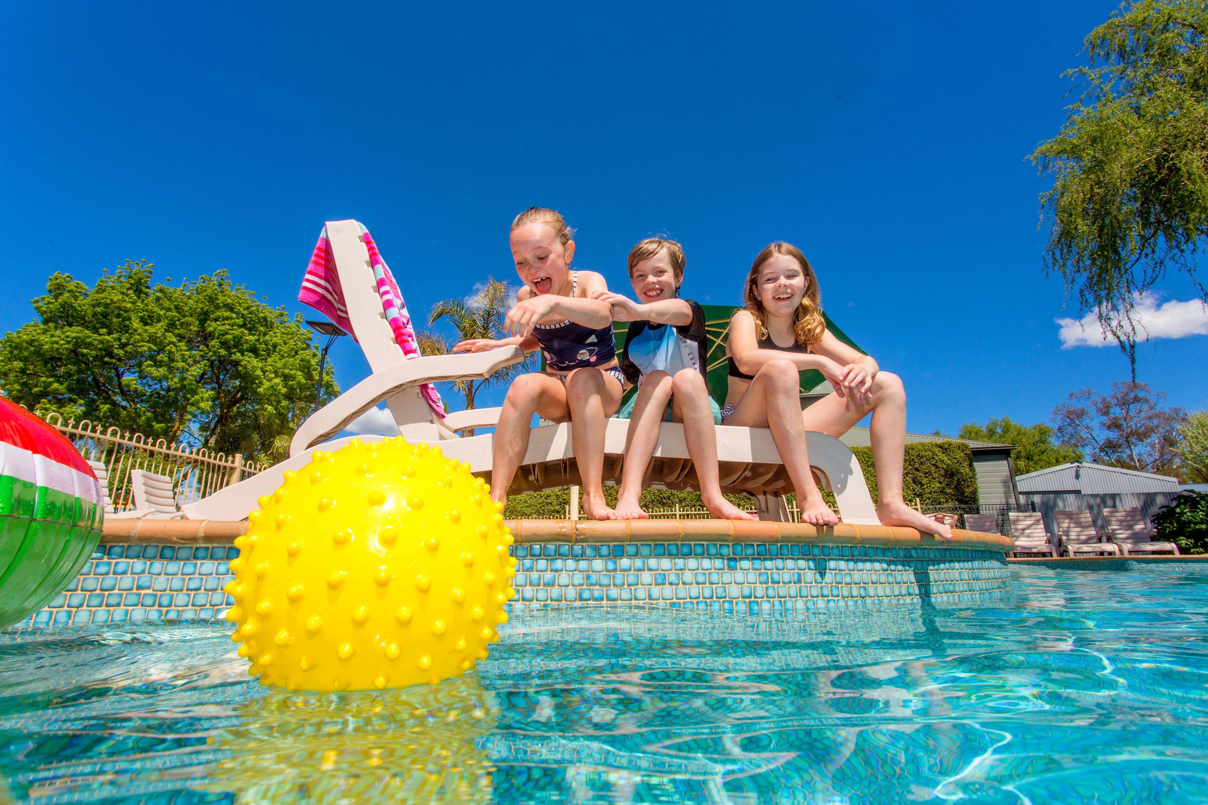 A poolside area with a clear blue sky, a pool, and lounge chairs.