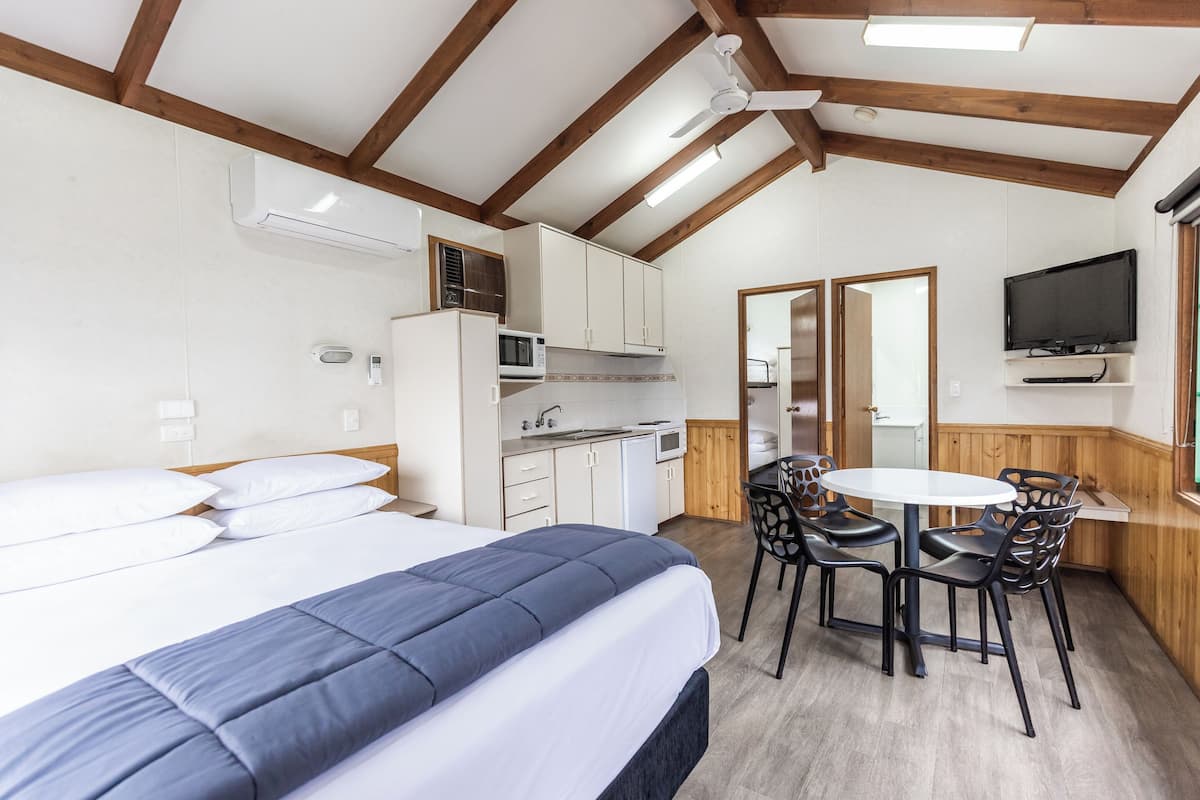 A bedroom with a bed, a kitchenette, a dining area with chairs, and a television mounted on the wall.