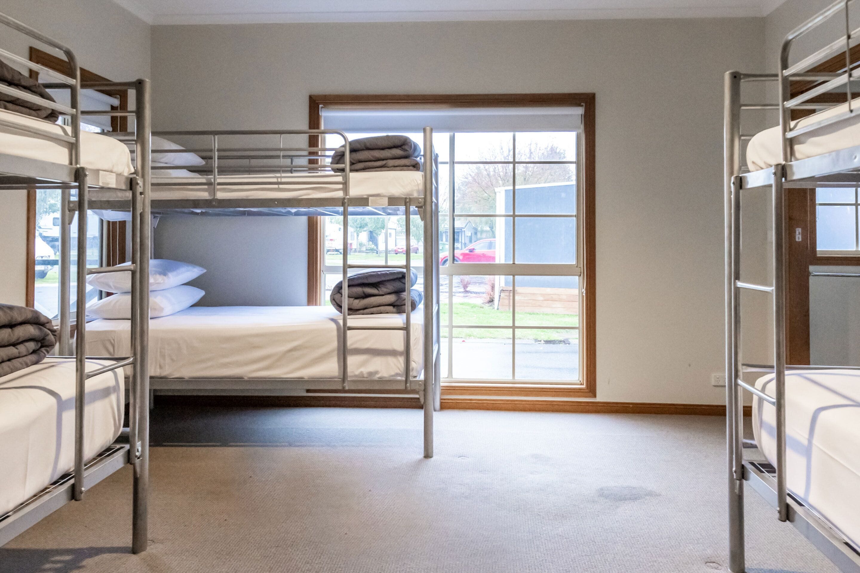 A dormitory room with bunk beds, a window with a view of the outside, and a carpeted floor.
