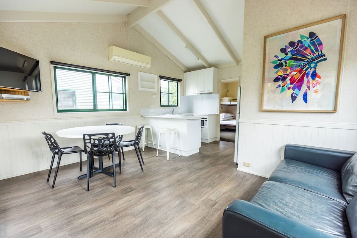 A modern kitchen with white cabinets, a dining area with a round table and chairs, and a blue leather sofa.