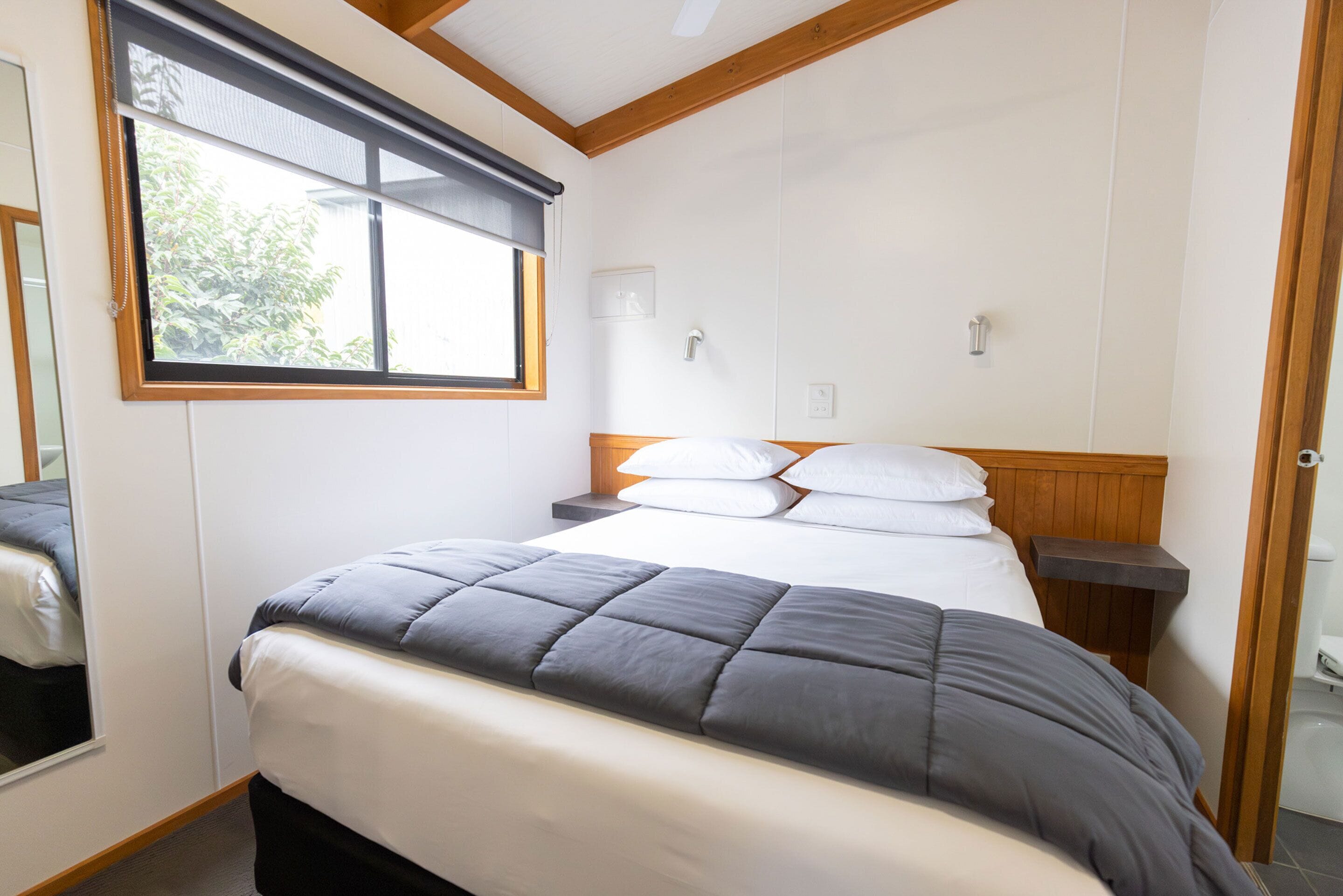 Un dormitorio con cama, mesita de noche, ventana y puerta.