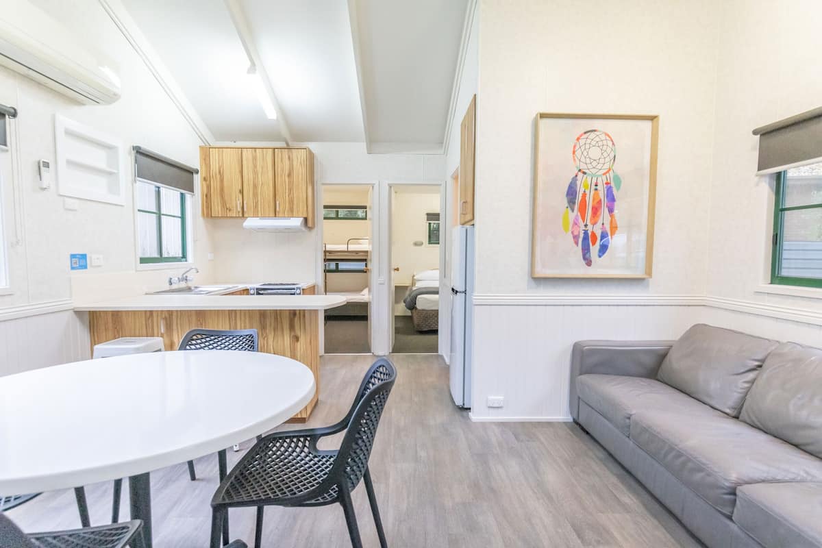A modern kitchen with wooden cabinets, a white countertop, and a dining area with a round table and chairs.