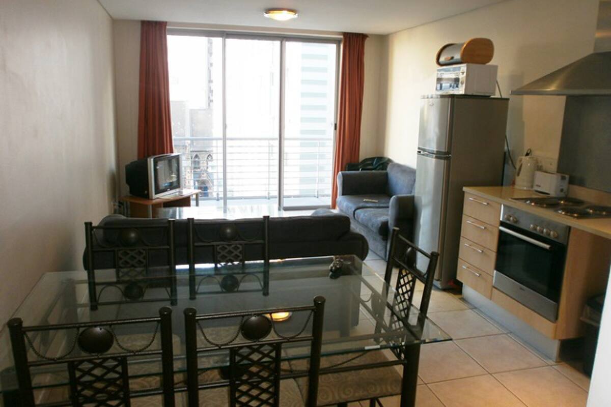 A modern apartment with a dining area, a living room, a kitchen, and a balcony with a city view.