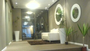 A modern living room with a white sofa, a large mirror, and a staircase leading to an upper level. - Greenmarket Place Apartments (Cape Town)