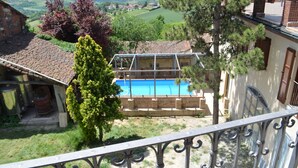 A pool with a clear blue water, surrounded by a brick pool deck, and a view of a rural landscape with fields and trees. - Relais San Desiderio (Calliano)