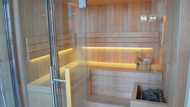 A sauna with wooden benches, a wooden bench with a bowl, and a small wooden box with stones. - Relais San Desiderio (Calliano)