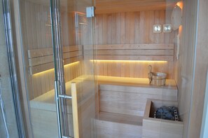 A sauna with wooden benches, a wooden bench with a bowl, and a small wooden box with stones. - Relais San Desiderio (Calliano)