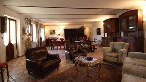 A spacious living room with a fireplace, leather armchairs, a coffee table, and a dining area with a chandelier. - Relais San Desiderio (Calliano)