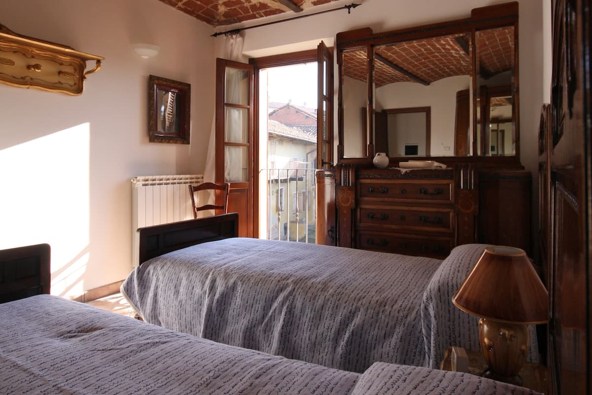 A room with two beds, a wooden dresser, a mirror, and a window with a view of a building outside.