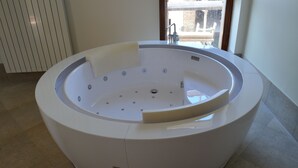 A modern, round jacuzzi tub with a built-in seat, positioned in a spacious room with a large window. - Relais San Desiderio (Calliano)