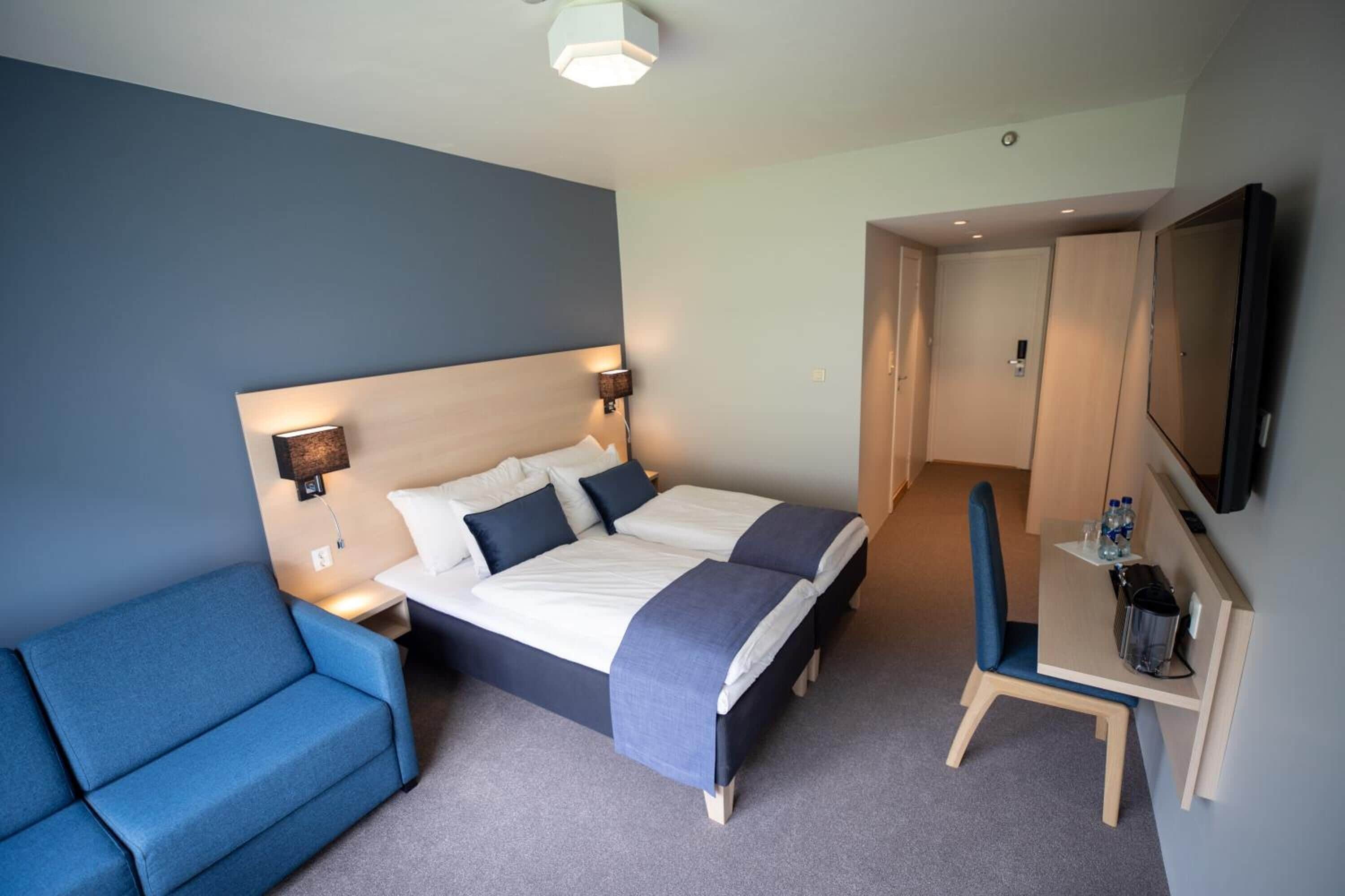 Una habitación de hotel con cama, escritorio, silla, sofá y televisor.