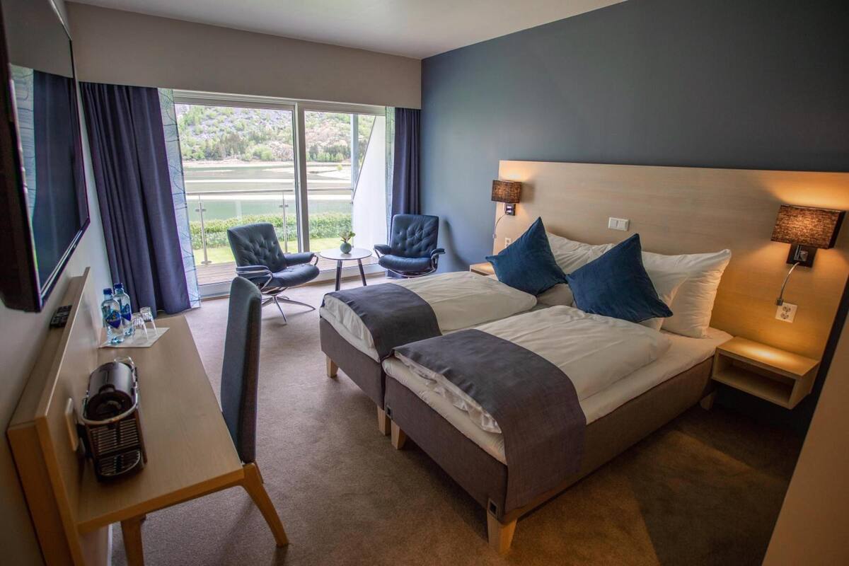 A hotel room with two beds, a desk, a chair, and a view of a lake.
