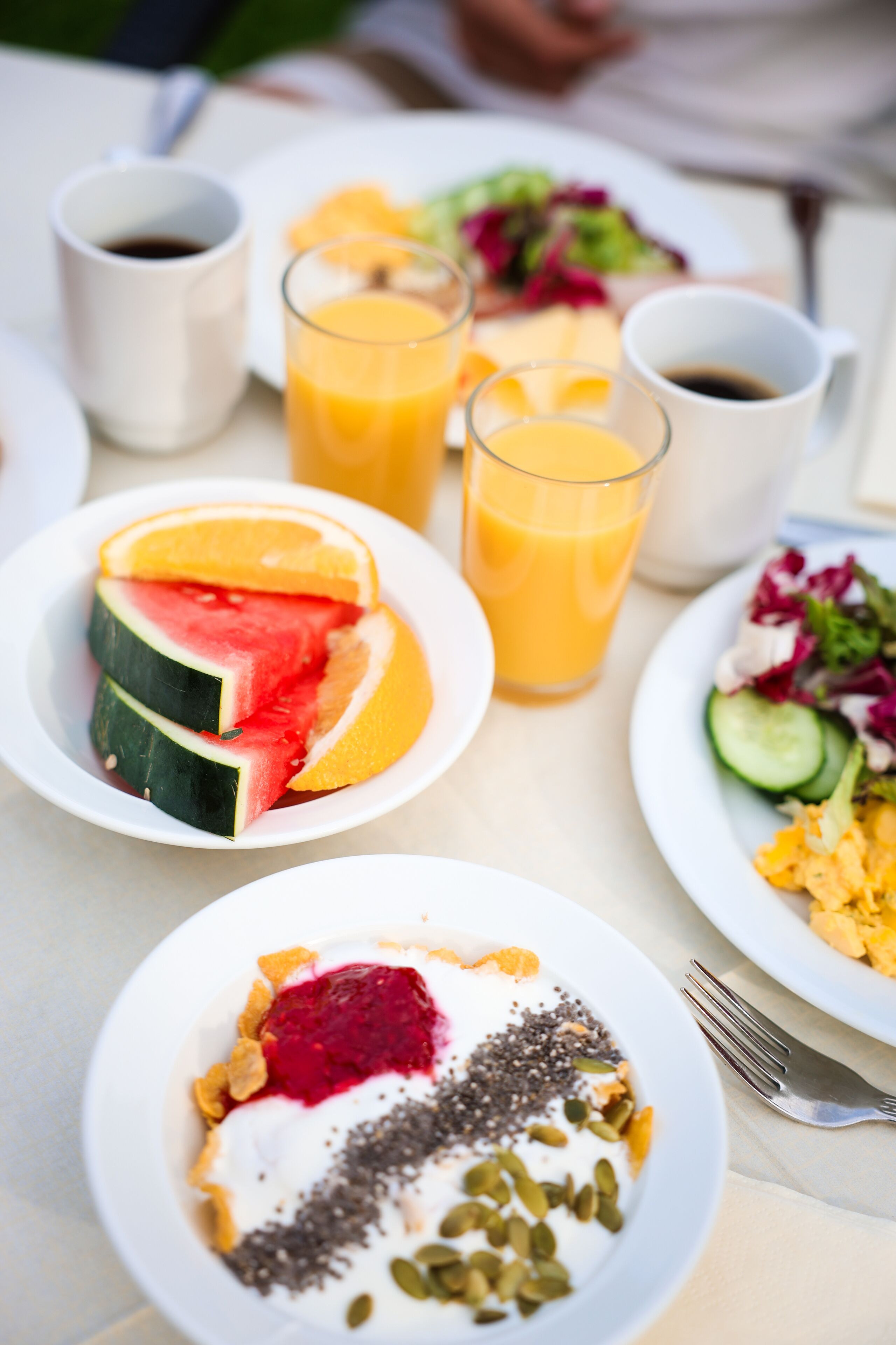 Une table dressée pour le petit-déjeuner, avec des assiettes remplies de nourriture, notamment de la pastèque, du jus d’orange et une salade.