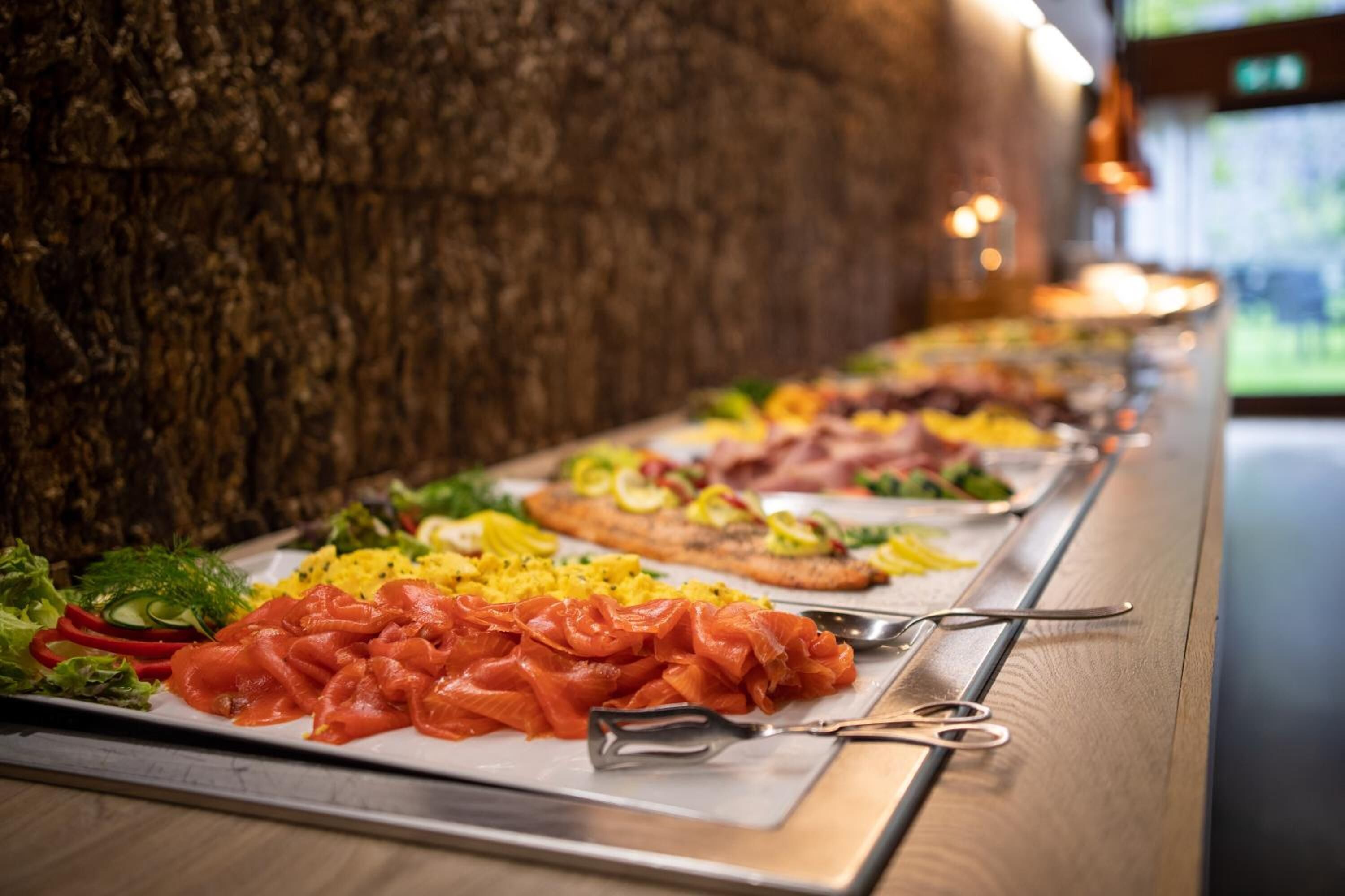 A buffet with various food items including smoked salmon, scrambled eggs, and vegetables.