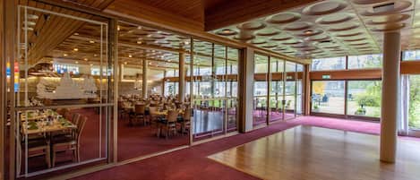 A spacious interior with wooden ceiling panels, large windows, and a red carpeted floor.