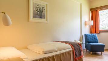 Une chambre d’hôtel avec un lit, une chaise, une table de chevet, une lampe et une fenêtre avec des rideaux.