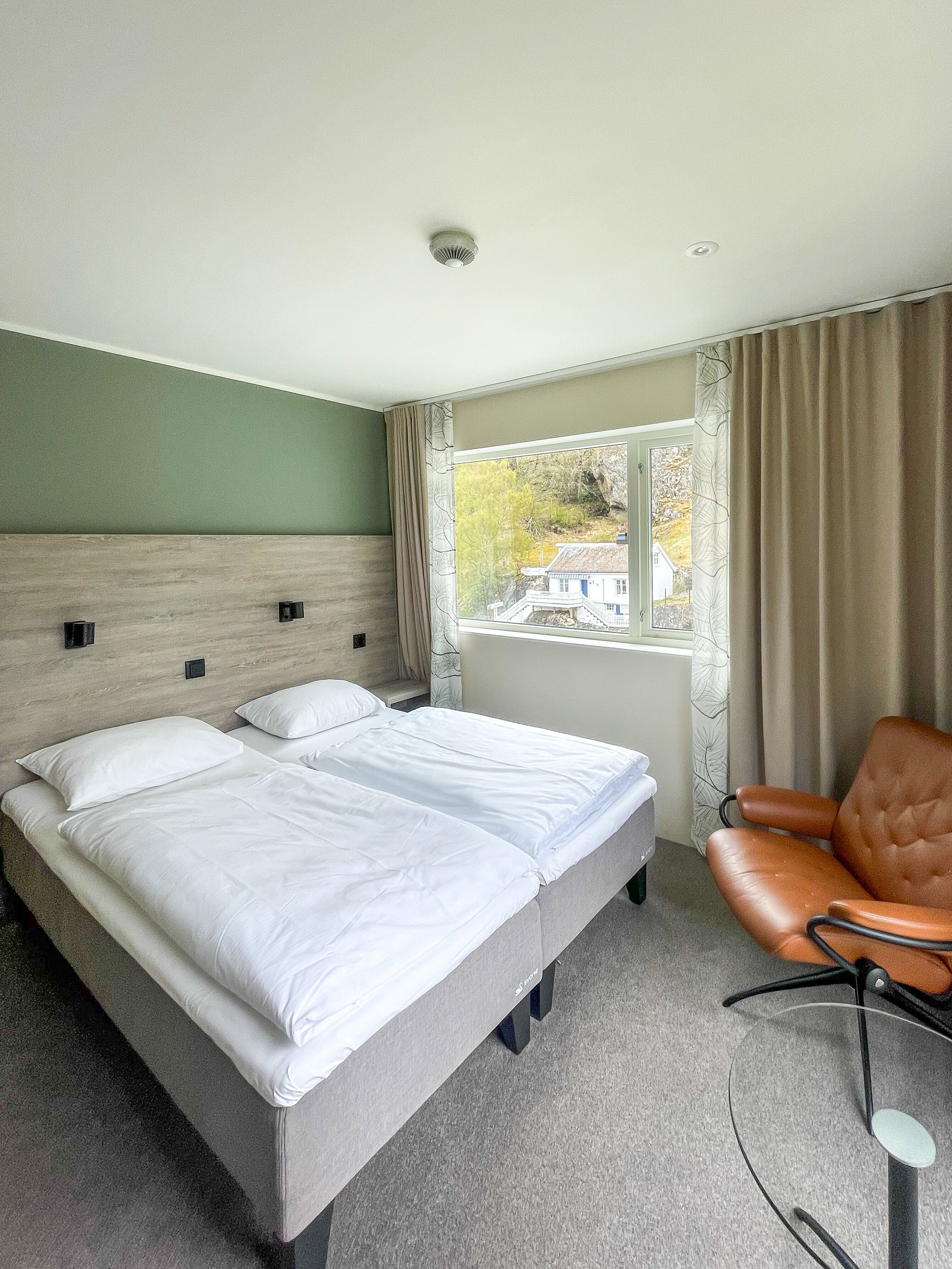 A hotel room with a bed, a chair, a window with a view, and a ceiling light.